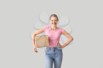 Young woman with cardboard box on light background�