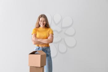 Young woman with cardboard boxes on light background�