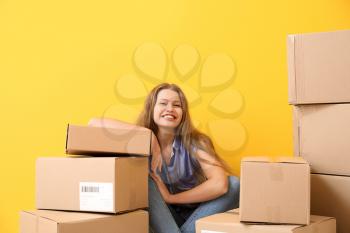 Young woman with many cardboard boxes near color wall�
