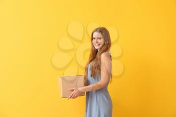 Young woman with cardboard box on color background�