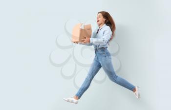 Jumping woman with cardboard box on light background�