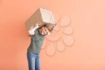 Young man with heavy cardboard box on color background�