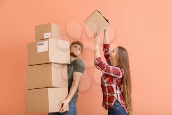 Young couple with many cardboard boxes on color background�