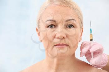 Mature woman and hand of plastic surgeon with syringe on light background�