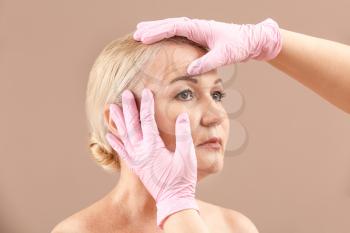 Plastic surgeon touching face of mature woman on color background�