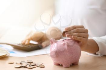 Young woman putting coin in piggy bank on table, closeup�
