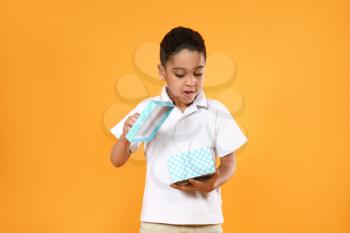 Portrait of cute little boy with gift box on color background�