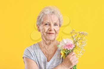 Portrait of senior woman with bouquet of flowers on color background�