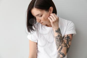 Stylish tattooed woman on light background�