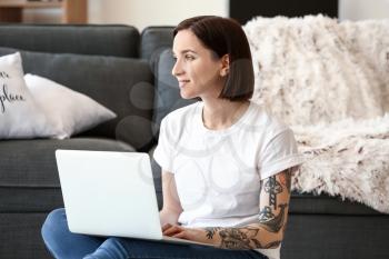 Beautiful tattooed woman working on laptop at home�