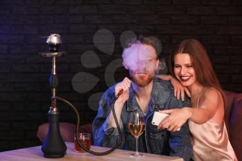 Young couple taking selfie while smoking hookah in cafe�