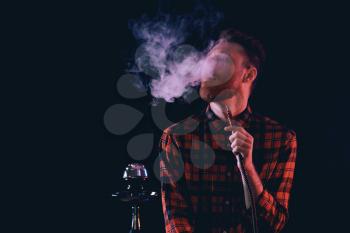 Young man smoking hookah on dark background�