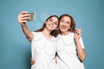 Portrait of happy mother with her daughter taking selfie on color background�