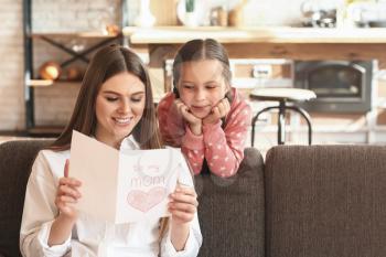 Happy mother receiving greeting card from her little daughter at home�