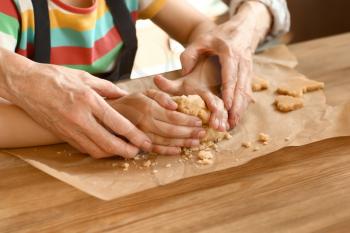 Little girl with her grandmother cooking cookies at table, closeup�
