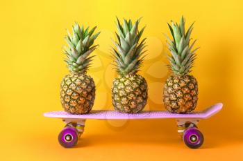 Ripe pineapples and skateboard on color background�