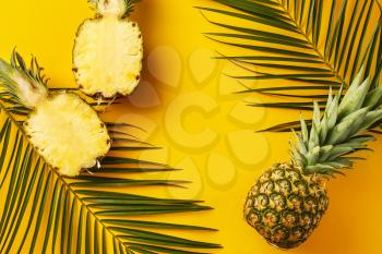 Ripe pineapples and palm leaves on color background�