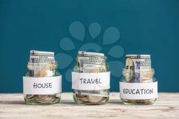 Jars with money for different needs on table against color background�