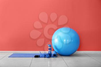 Set of sports equipment with fitness ball and bottle of water near color wall�
