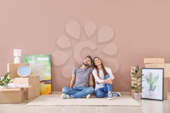 Young couple with belongings sitting near color wall in their new house�