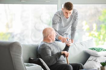 Male caregiver giving glass of water to senior man in nursing home�