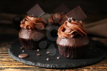 Slate plate with tasty chocolate cupcakes on wooden table�