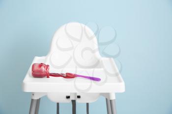 Overturned jar with tasty baby food on high chair against grey background�