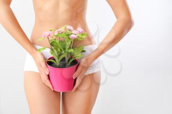Beautiful young woman with plant in pot on light background. Depilation concept�