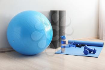 Set of sports equipment with fitness ball and bottle of water near light wall�