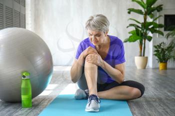 Sporty mature woman with injured knee after training at home�