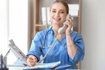 Young medical assistant talking by phone in clinic�