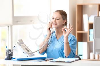 Young medical assistant talking by phone in clinic�