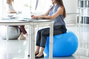 Young businesswoman sitting on fitball while working in office�