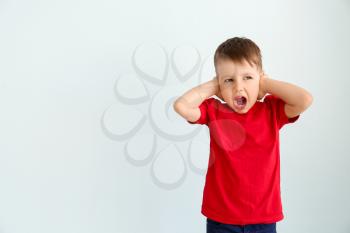 Screaming little boy with autistic disorder covering ears on light background�