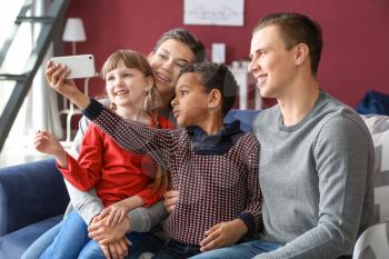 Happy couple with adopted children taking selfie at home�