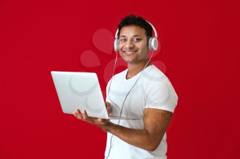 Handsome man with laptop and headphones on color background�