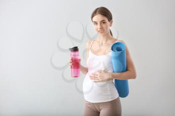 Beautiful pregnant woman with yoga mat and bottle of water on grey background�