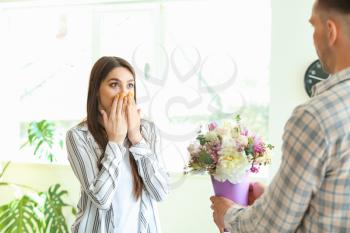 Husband greeting his wife with bouquet of flowers at home�