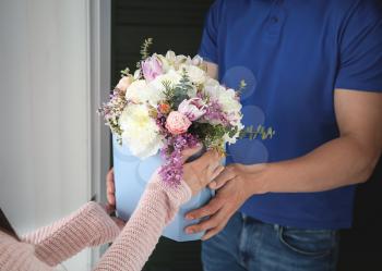 Young woman receiving beautiful flowers from delivery man at home�
