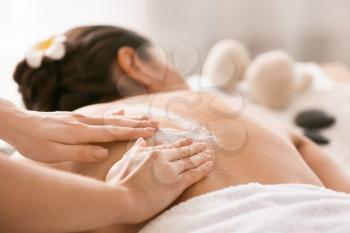 Young woman undergoing treatment with body scrub in spa salon�