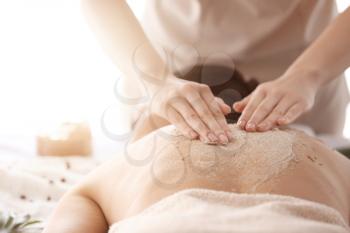 Young woman undergoing treatment with body scrub in spa salon, closeup�