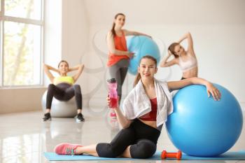 Young sporty woman with fitball drinking water in gym�