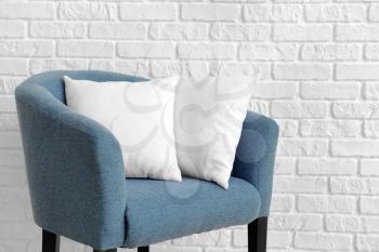 Soft pillows on armchair against white brick wall�