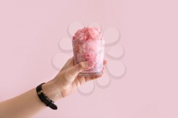 Female hand holding glass of tasty shaved ice on color background�
