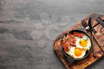 Frying pan with tasty eggs and bacon on grey background�