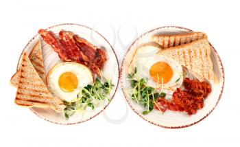 Plates with tasty fried eggs, bacon and toasts on white background�