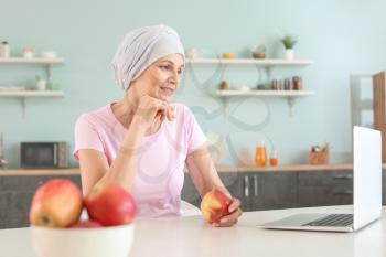 Mature woman after chemotherapy using laptop in kitchen at home�