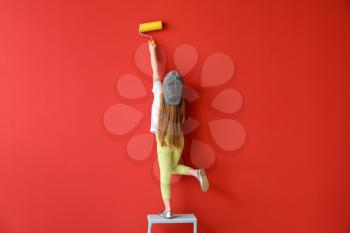 Cute little girl painting wall in room�