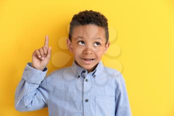 Cute African-American boy with raised index finger on color background�
