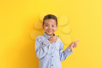 Cute African-American boy pointing at something on color background�